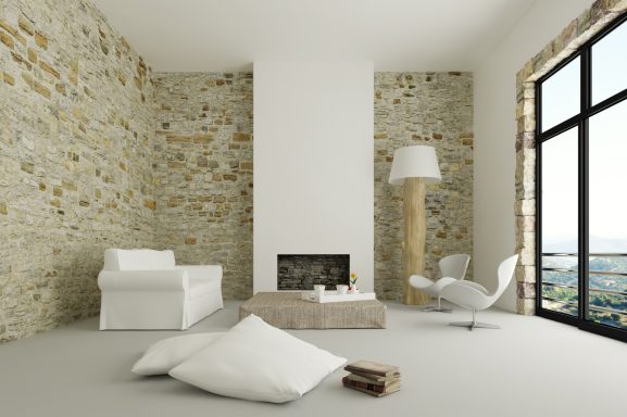 Helle, moderne Wohnraum mit Steinwänden, Sofa, Kamin und Blick auf die Landschaft.