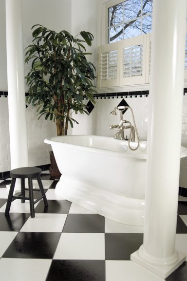 Elegante Badewanne aus Weiß mit schwarzen und weißen Fliesen, Pflanze und Hocker.