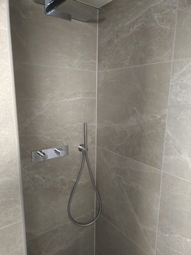 Dusche mit verchromter Armatur, dunklen, kleinformatigen Fliesen an der Vorderwand und Großformatfliesen (120&nbsp;×&nbsp;60) an den übrigen Wänden