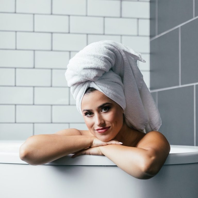 Eine Frau mit Handtuch auf dem Kopf lehnt lächelnd an einer Badewanne. Neue Fliesen, Badsanierung