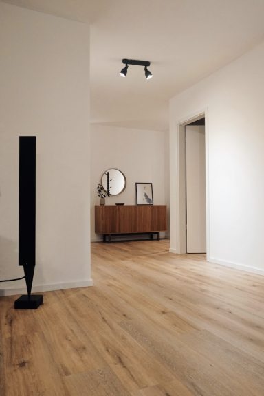 Heller Raum mit Holzfußboden, Spiegel, Kommode und einem schwarzen Stehlampe.