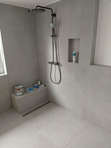 Dusche mit grauen Fliesen, Sitzbank und integrierter Wandnische