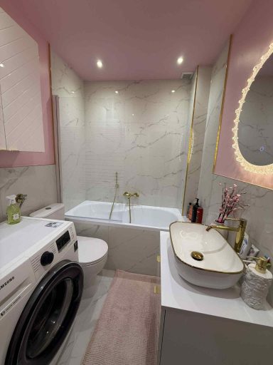 Modernes Badezimmer mit Fliesen in Marmoroptik, goldenen Details und rosa Wänden mit Spachtelarbeiten in Q4-Qualität
