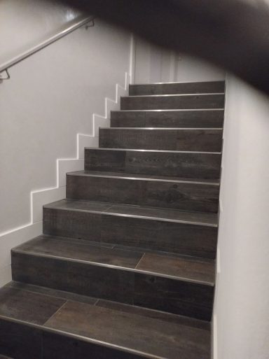 Treppe mit dunklen Fliesen in Holzoptik und weißem Sockel