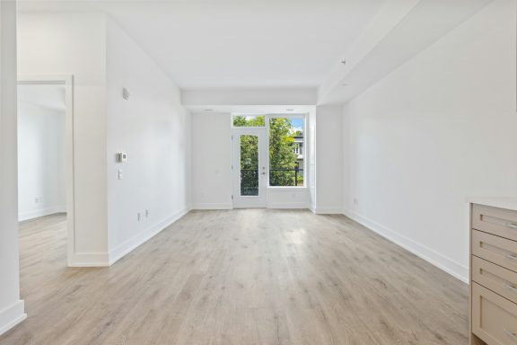 Leerer, heller Raum mit Vinyl-Laminat und großen Fenstern zur grünen Außenansicht.