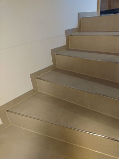 Treppe mit beigen Fliesen in Natursteinoptik und gefliestem Sockel