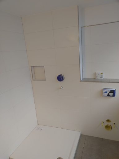 Bad mit Duschwanne, weißen Wandfliesen und grauen Fliesen an Ablage und Boden