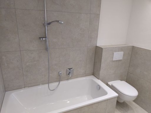 Badezimmer mit Badewanne und WC – Fliesen in heller Marmoroptik