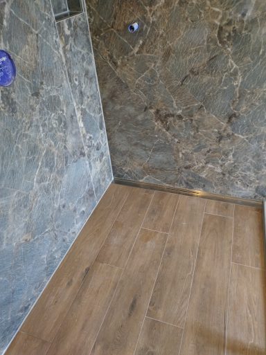 Dusche mit grauen Fliesenwänden und einem Holzoptik-Fliesen auf dem Boden 