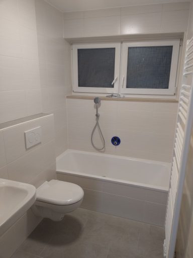 Klassisches Badezimmer mit hellen Wandfliesen, weißen Wänden in Q4-Spachtelqualität und grauen Bodenfliesen