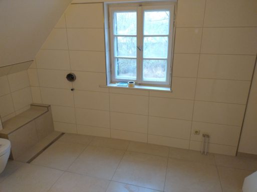 Badezimmer im Dachgeschoss nach Teilsanierung mit barrierefreier Dusche und Sitzbank sowie weißen Wandfliesen und beigen Bodenfliesen