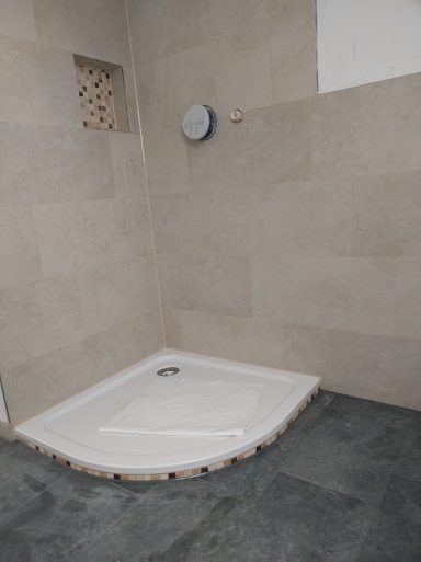 Badezimmer mit Dusche und Badewanne – helle Wandfliesen, dunklere Bodenfliesen und Mosaik in der Dusch­nische