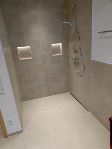 Moderne Dusche mit beige Fliesen und zwei eingelassenen Lichtquellen.