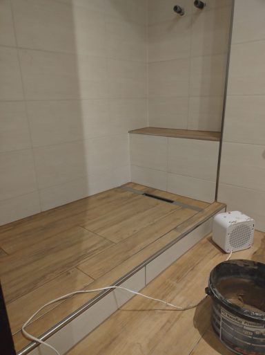 Dusche mit hellen Wandfliesen, Glasprofil für eine Duschwand und Bodenfliesen in Holzoptik