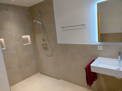 Barrierefreie Dusche mit Nische und Beleuchtung – helle Fliesen in Marmoroptik